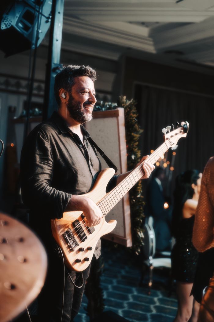 A male bassist performs with joy on stage during an indoor music event.