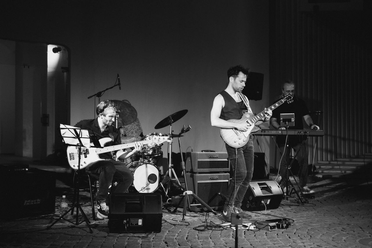 About A dynamic black and white photo of a live jazz band performing with guitar, bass, and piano on stage.